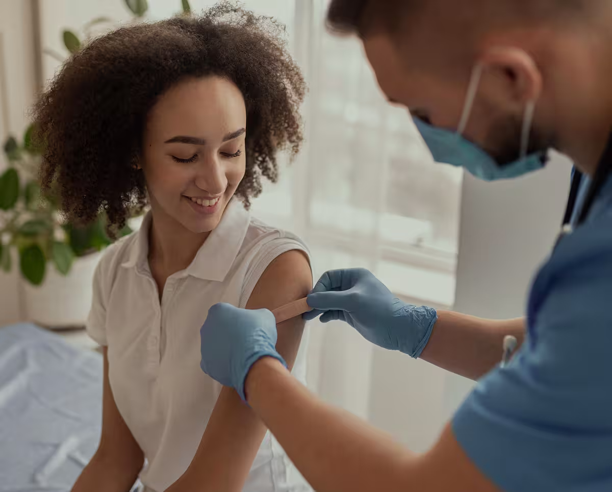 Healthcare worker applying a bandage to a smiling woman’s upper arm after a vaccination