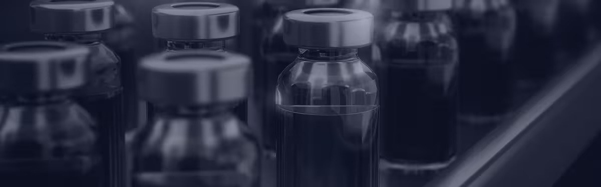 Close-up of vaccine vials with silver caps on a production line, shown in navy blue tones.
