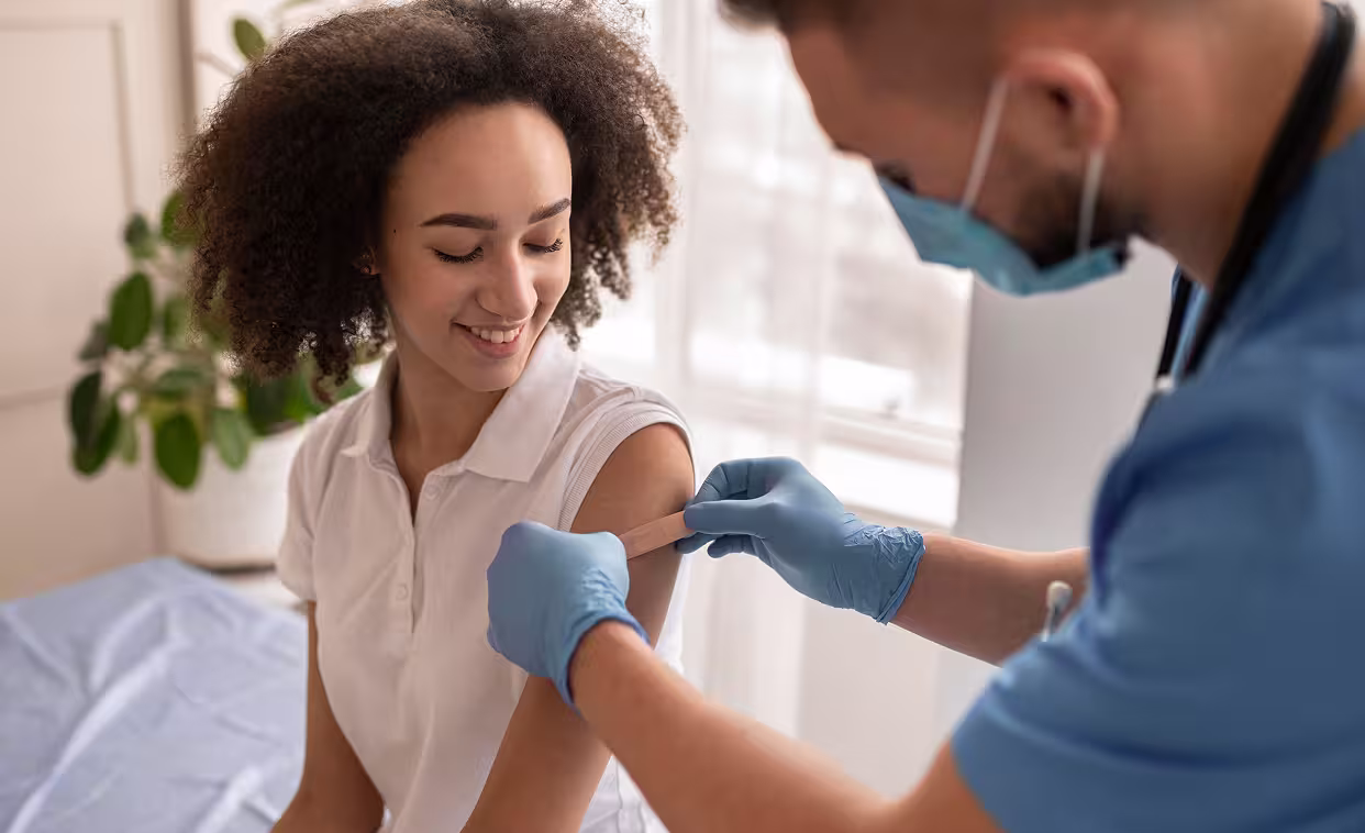 Healthcare worker applying a bandage to a smiling woman’s upper arm after a vaccination