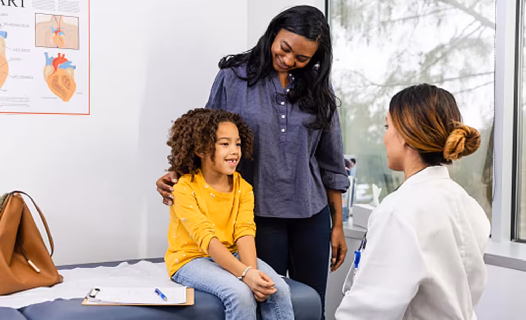 A child sits on an exam table with her mother and doctor during a medical visit