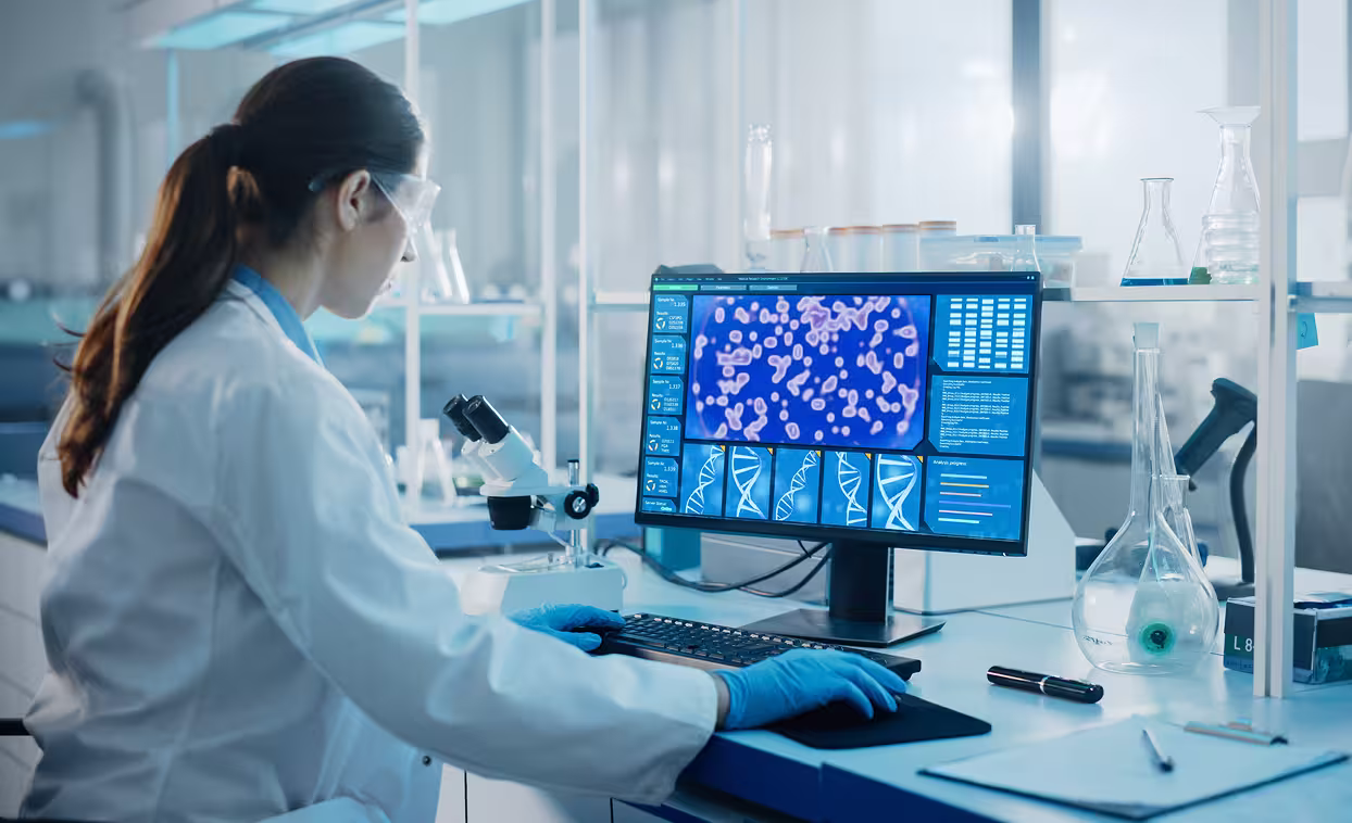 Scientist in a lab coat and safety goggles working at a computer in a laboratory