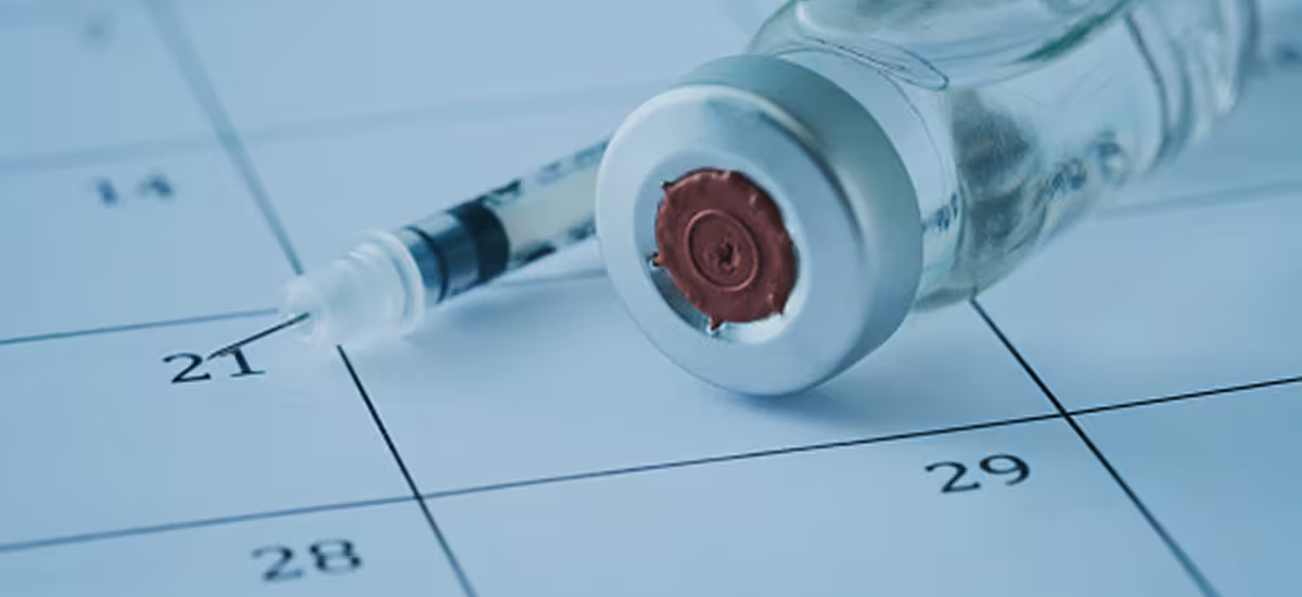 Vaccine vial and syringe on a calendar, representing vaccination scheduling